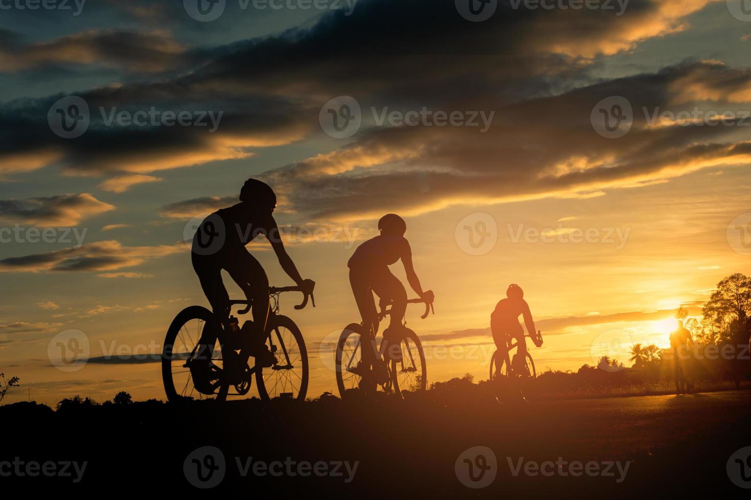 The men ride  bikes at sunset with orange-blue sky background. Abstract Silhouette background concept. photo