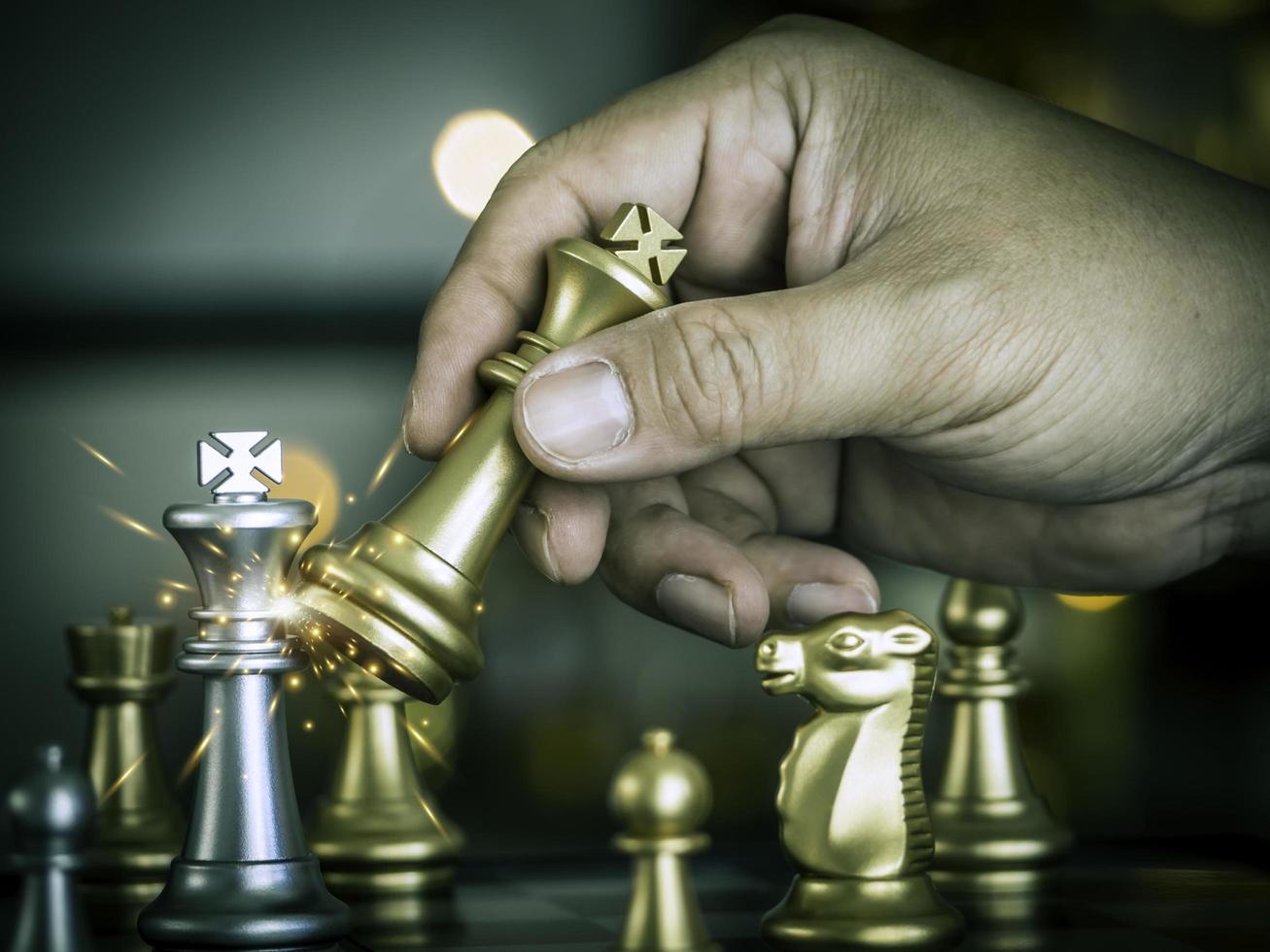 Hand businessman moving the golden king chess fighting silver king with fire sparks chess on chess board to successfully in the competition. Management or leadership strategy and teamwork concept. photo