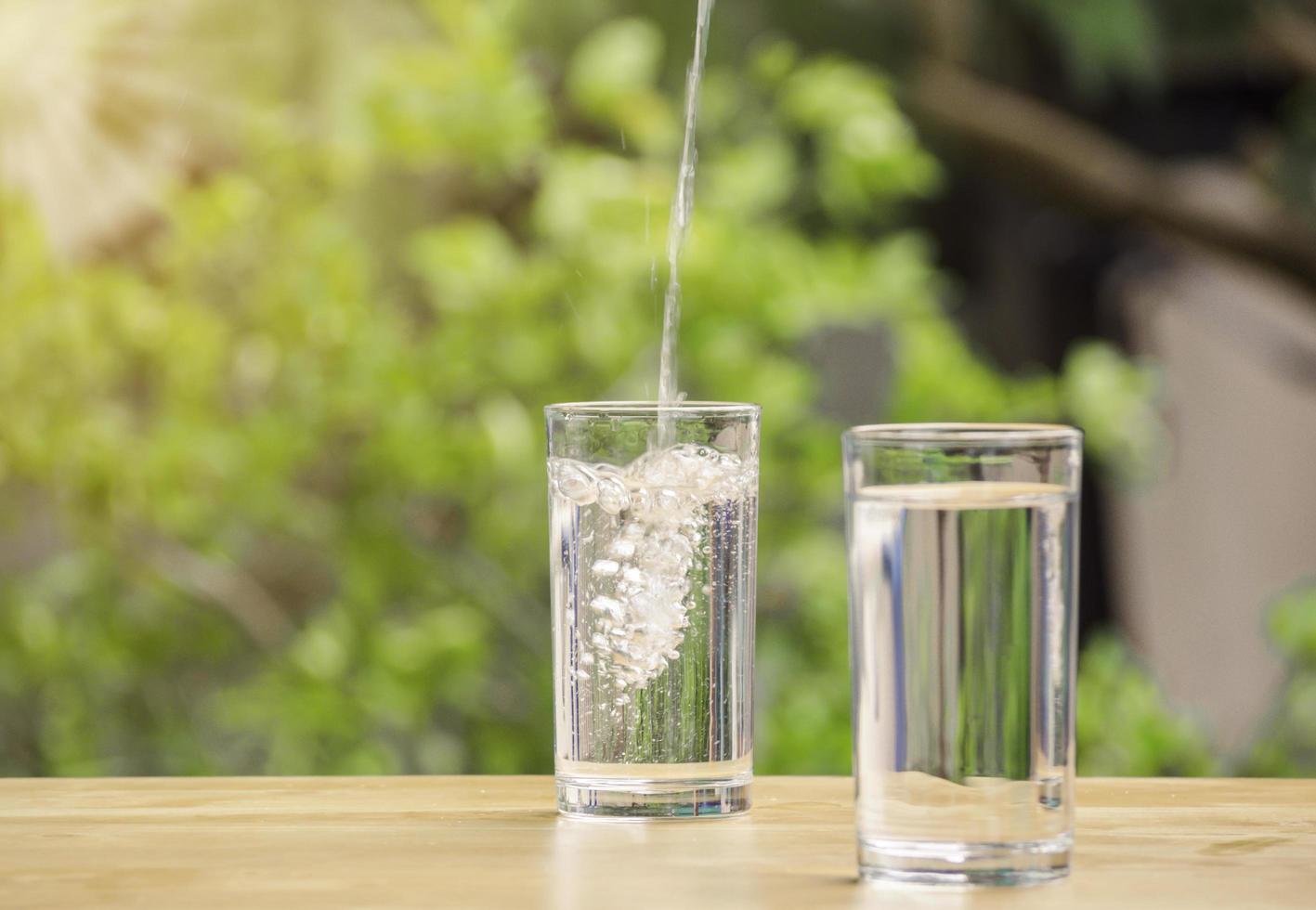 The pure water from jug into glass on wooden table on nature background. photo