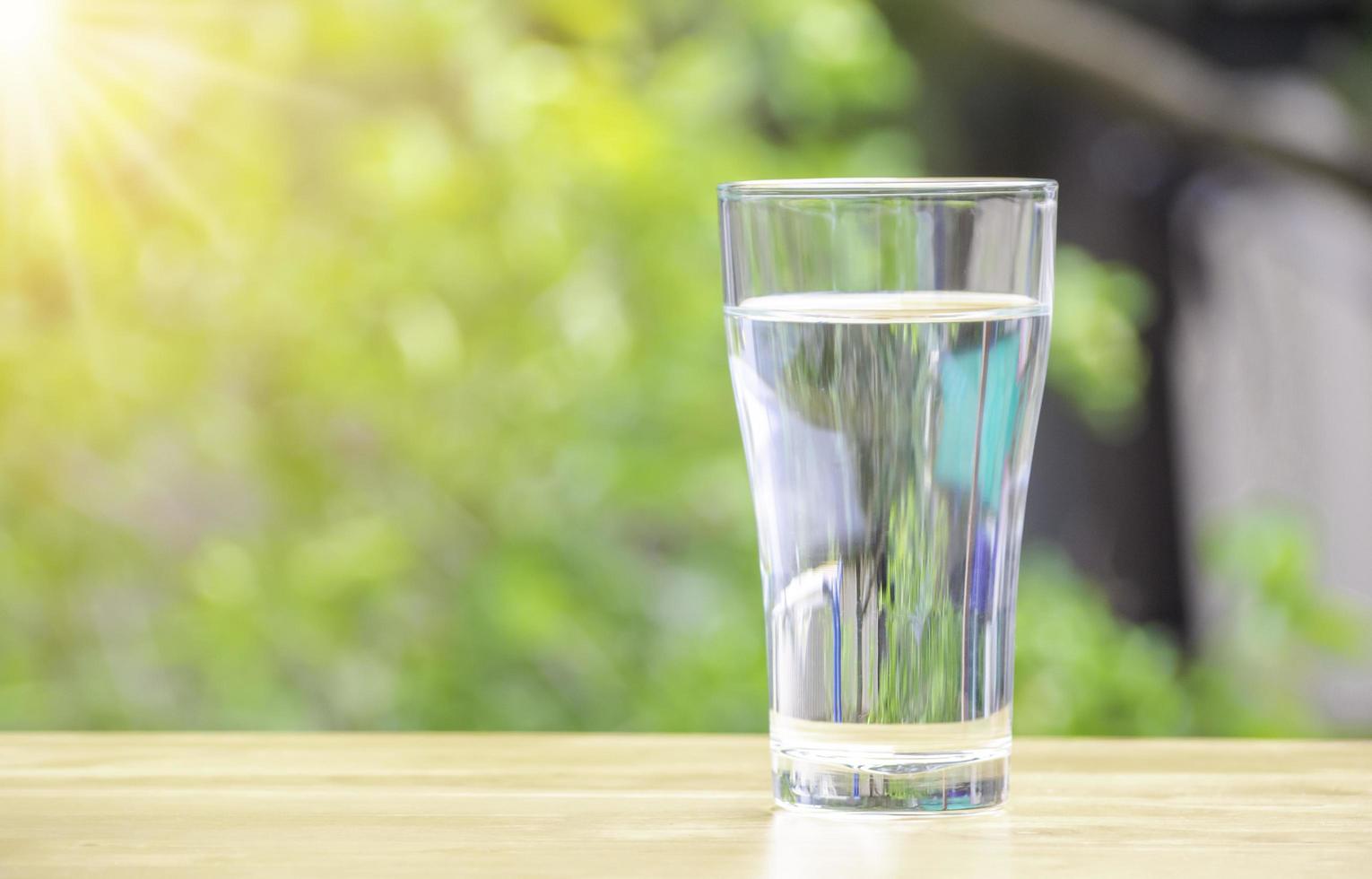 The pure water from jug into glass on wooden table on nature background. photo