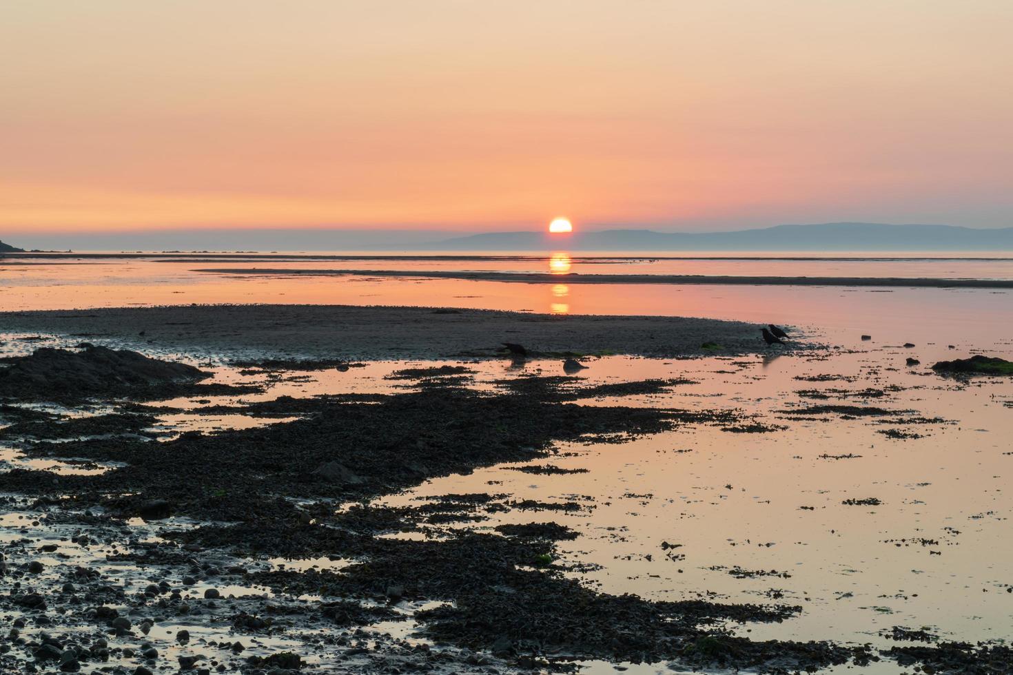 puesta de sol sobre la playa detrás de la montaña. colorida línea horizontal reflejo del sol en el agua, espejo. foto