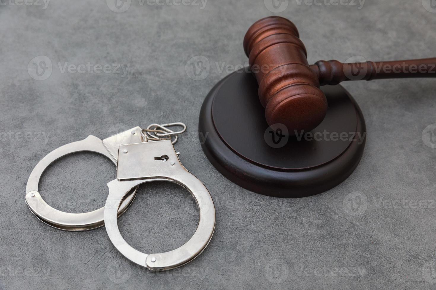 Law theme. Court of law trial in session. Judge gavel handcuffs on grey table in lawyer office or court session. Mallet of judge on concrete stone grey background. Justice human rights concept. photo