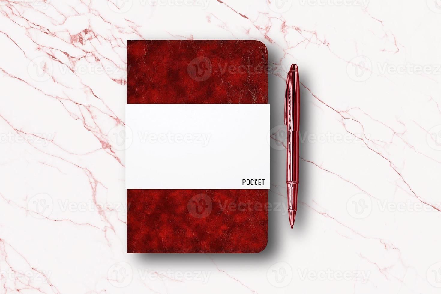 Blank red paper notebook or pocket book and a pen on white marble table background. photo