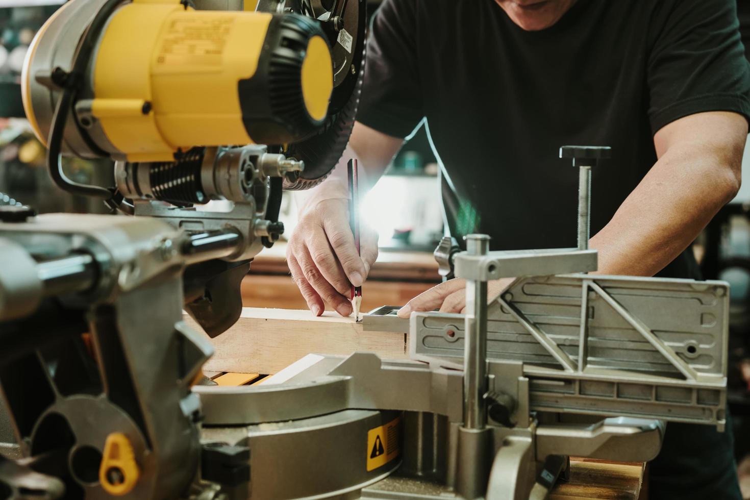 el carpintero usa escuadra de maquinista y marcas de lápiz en la madera en la mesa de sierra de inglete en el taller, el fabricante de bricolaje y el concepto de carpintería. enfoque selectivo foto