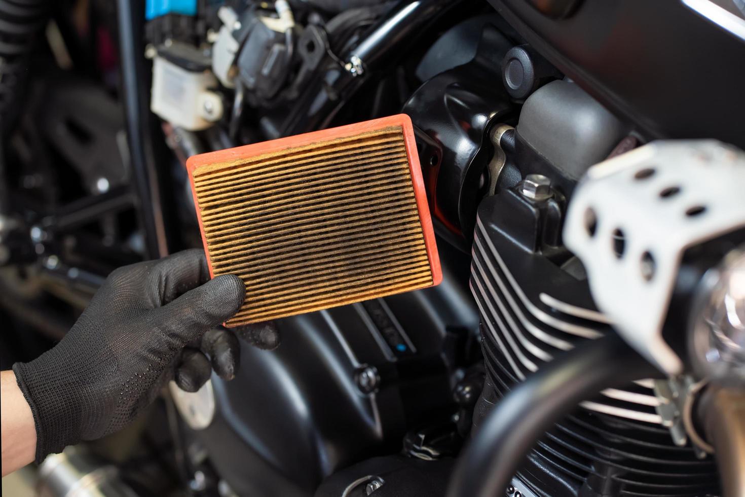 mechanic holding dirty Engine Air Filter over motorcycle, working in motorcycle garage. Repair service and maintenance concept photo