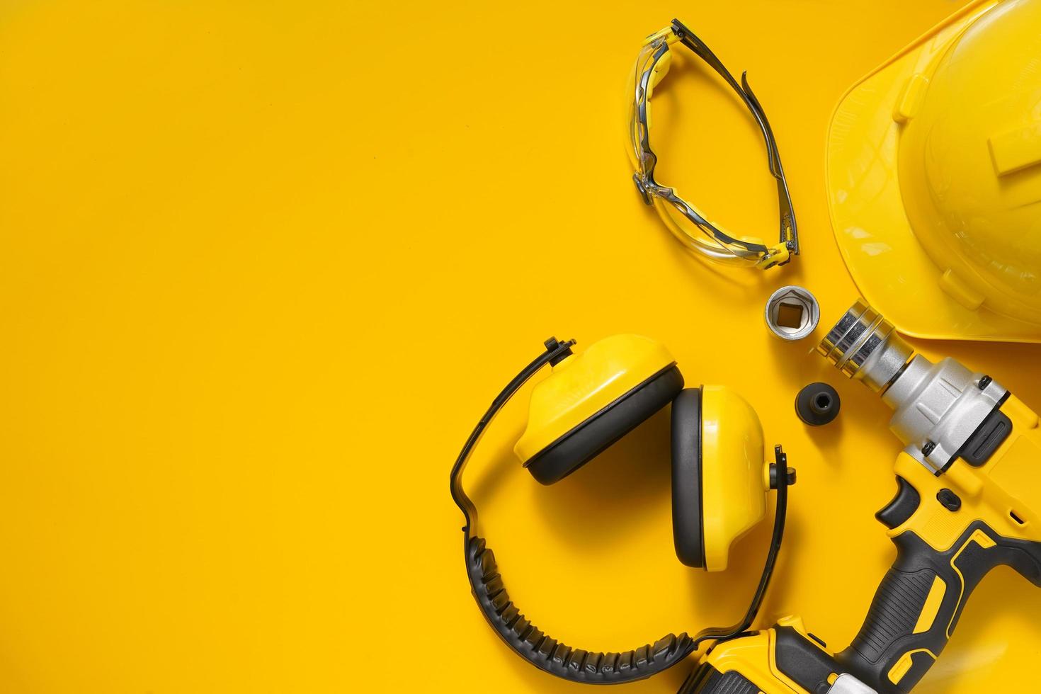 Ear Muffs, Mid-Range Cordless Impact Wrench and Safety glasses , Helmet on yellow background .Safety Equipment concept . photo