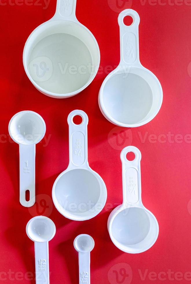 juego de tazas blancas de medida, uso de cucharas de medida en la cocina sobre fondo rojo de madera en la vista superior foto