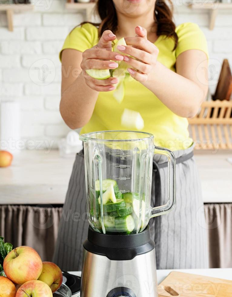 mujer joven haciendo batido de pepino verde en la cocina de casa foto