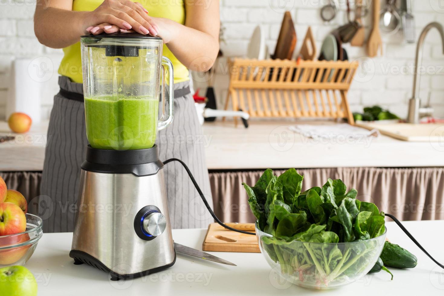 mujer joven haciendo batido verde en la cocina de casa foto