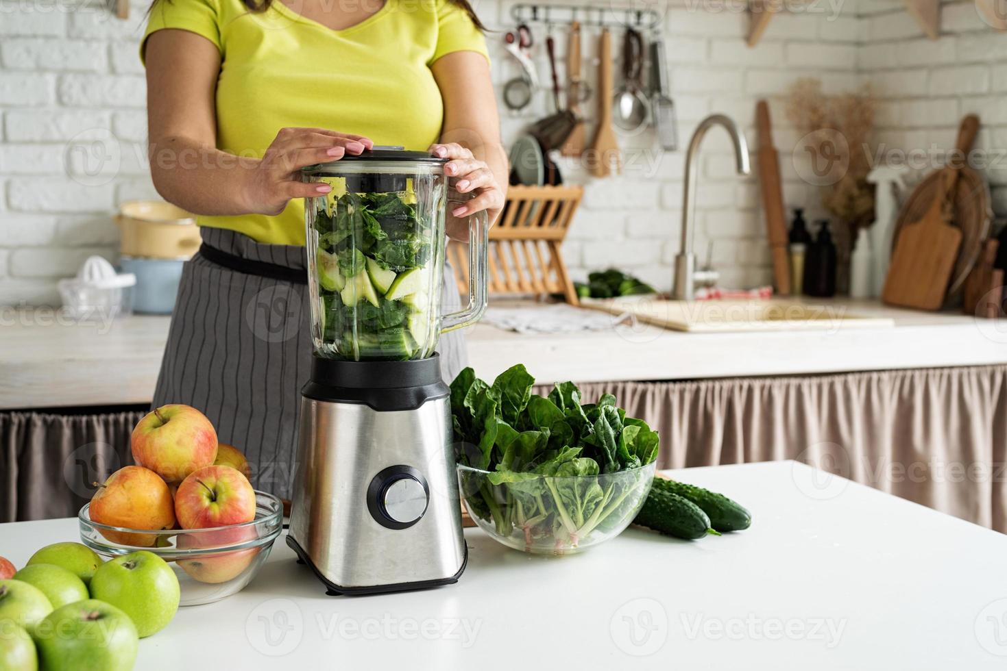 mujer joven haciendo batido verde en la cocina de casa foto