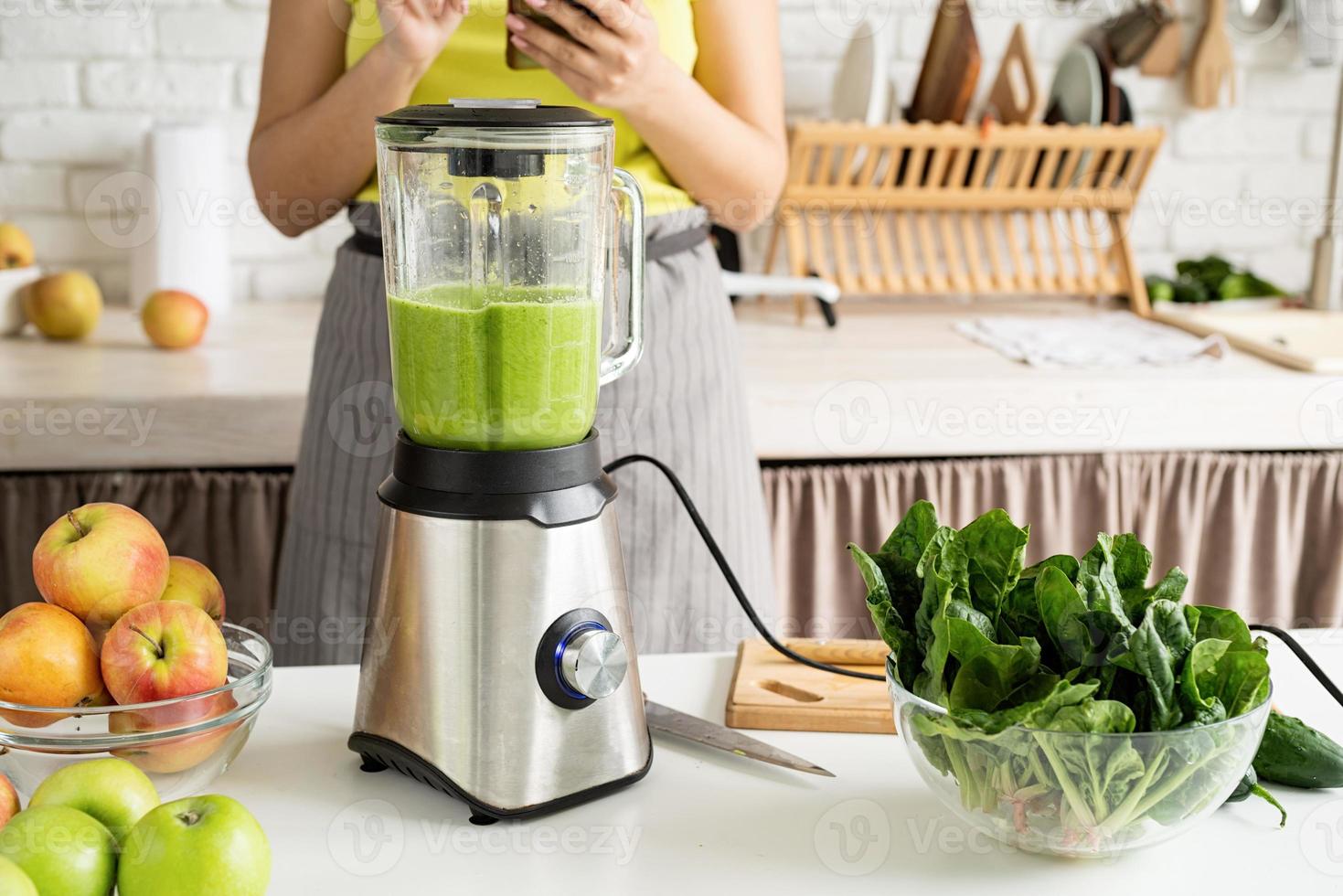Young woman making green smoothie at home kitchen photo