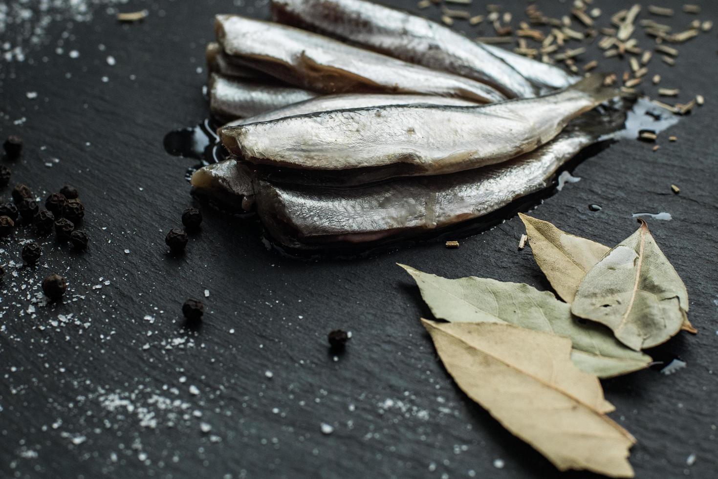 Fresh oiled sardines on black table with spices photo