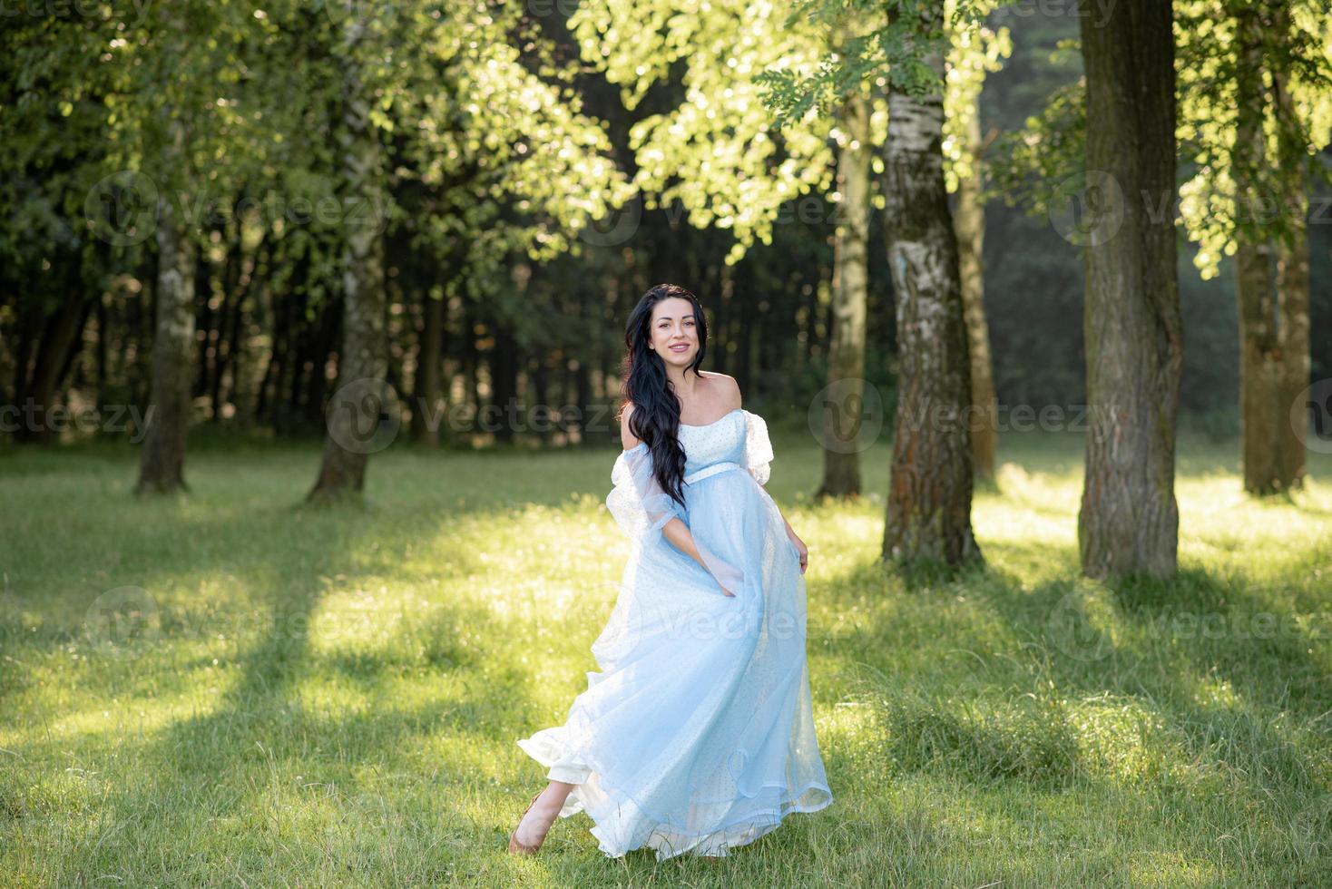 Pregnant woman in a hat posing in a dress on a background of green trees. photo