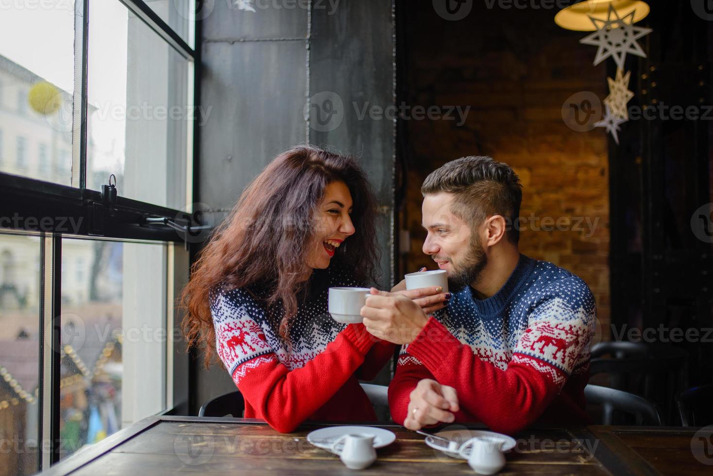 pareja feliz y romántica en suéteres cálidos beben café de vasos de papel desechables en la cafetería. vacaciones, navidad, invierno, amor, bebidas calientes, concepto de personas foto