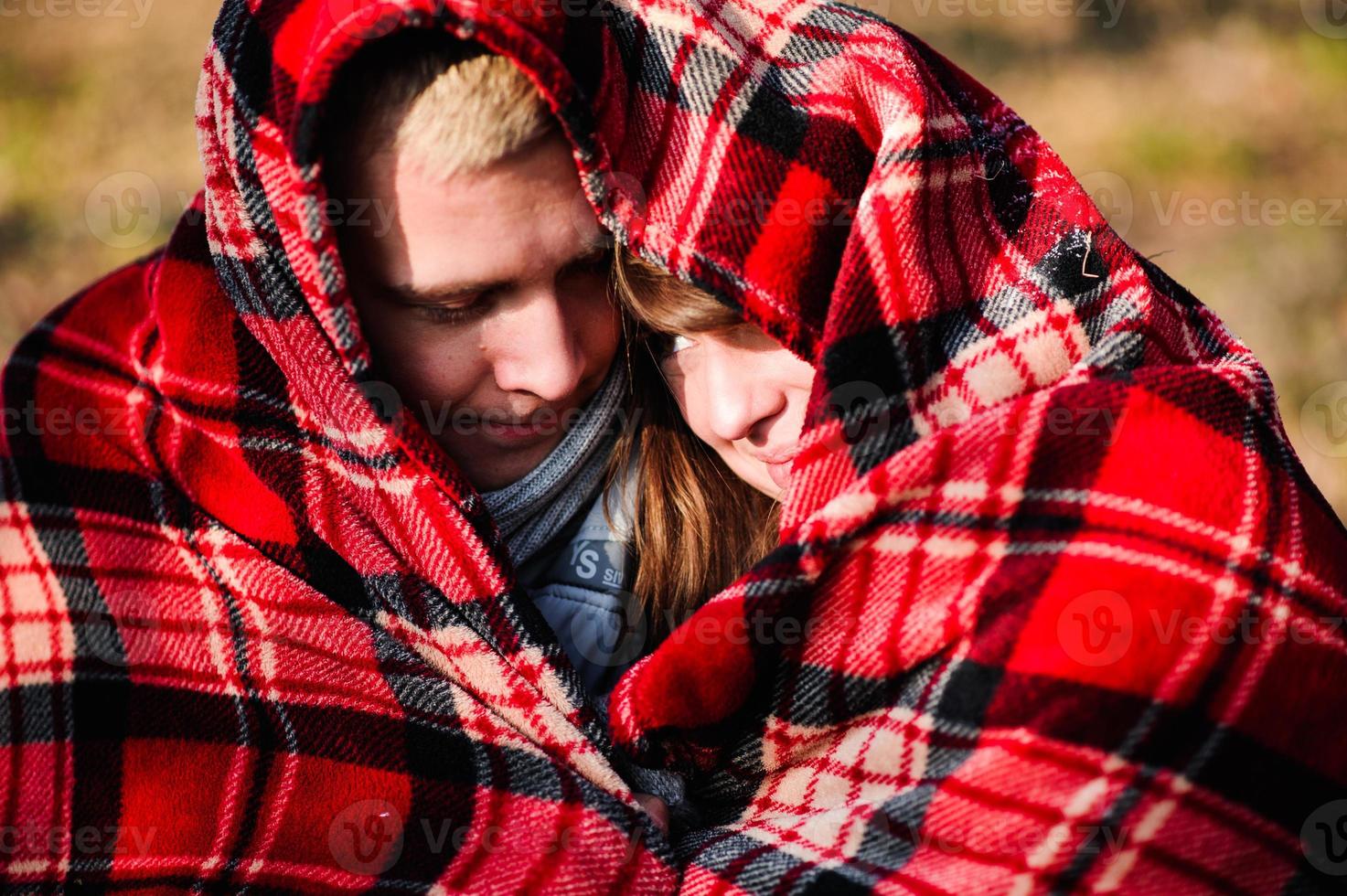 Young loving couple dressed in blue sweater sitting with red coffee cups on the firewood in winter forest photo