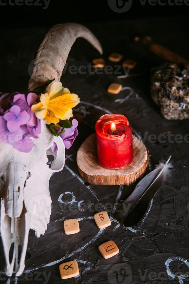 scull de cabra blanca con cuernos, flores, libro viejo abierto, velas en la mesa de brujas. foto