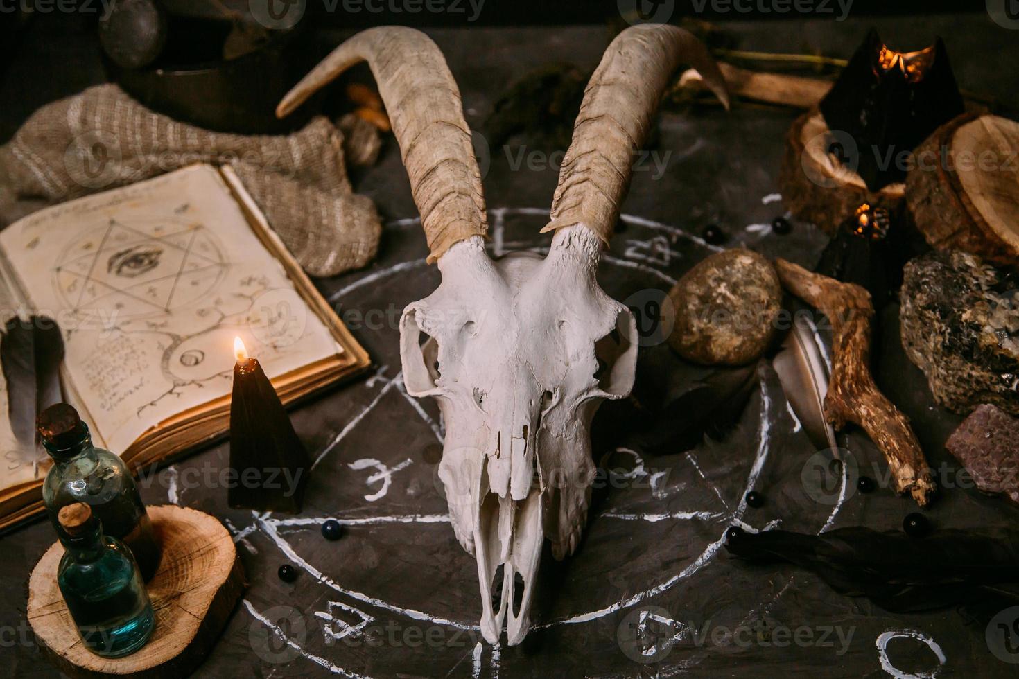 White goat scull with horns, open old book, magic spells, runes, black candles photo