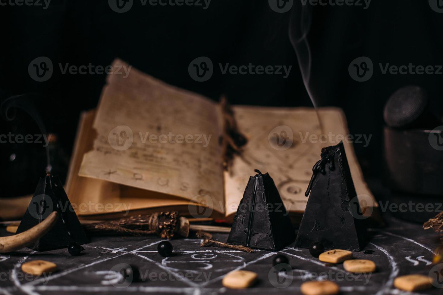 Open old book with magic spells, runes, black candles on witch table. Occult, esoteric, divination and wicca concept. photo