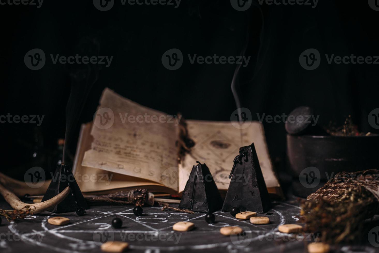 Open old book with magic spells, runes, black candles on witch table. Occult, esoteric, divination and wicca concept. photo