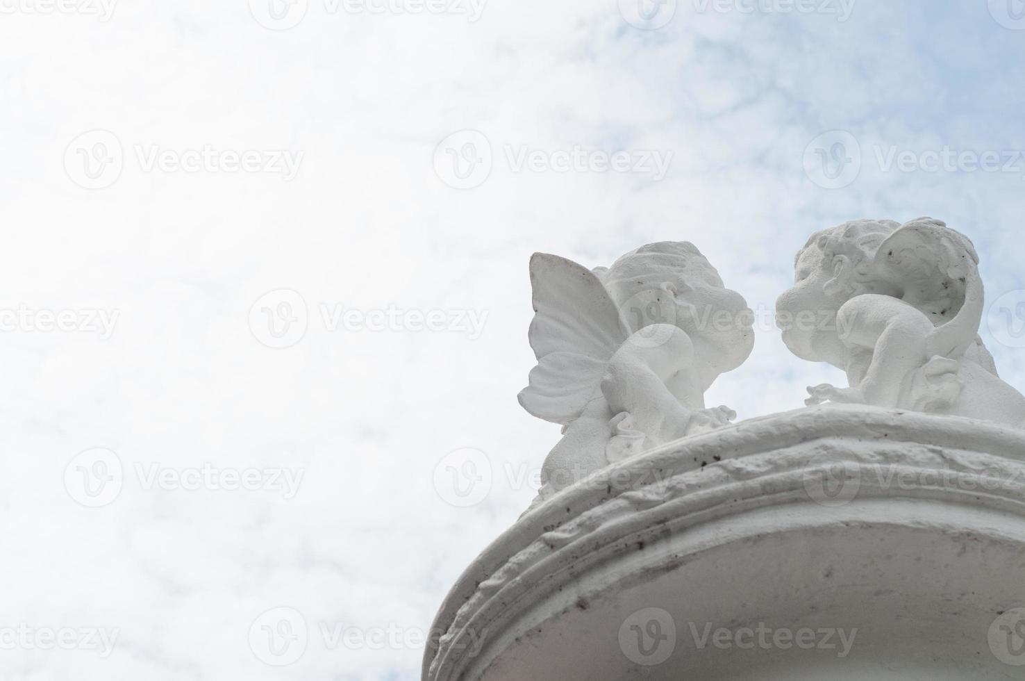 Two cute child angels kissing on the light blue sky photo