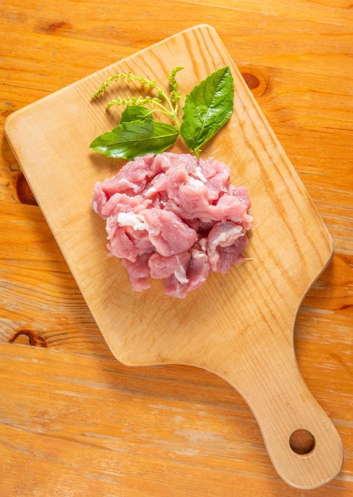 carne de cerdo cruda picada en una tabla de cortar de madera y hojas de albahaca foto