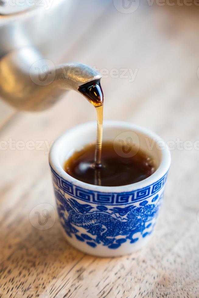 el té se vierte sobre el vaso de azulejos de la tetera. foto