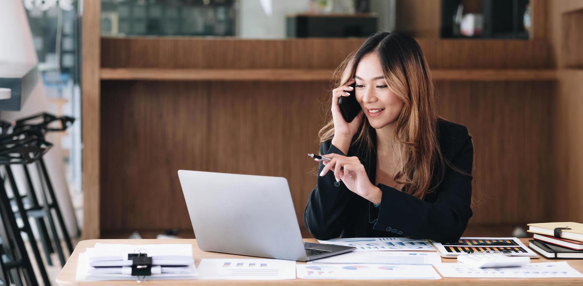 mujer de negocios asiática tiene la alegría de hablar por teléfono, computadora portátil y tableta en el escritorio de la oficina. foto