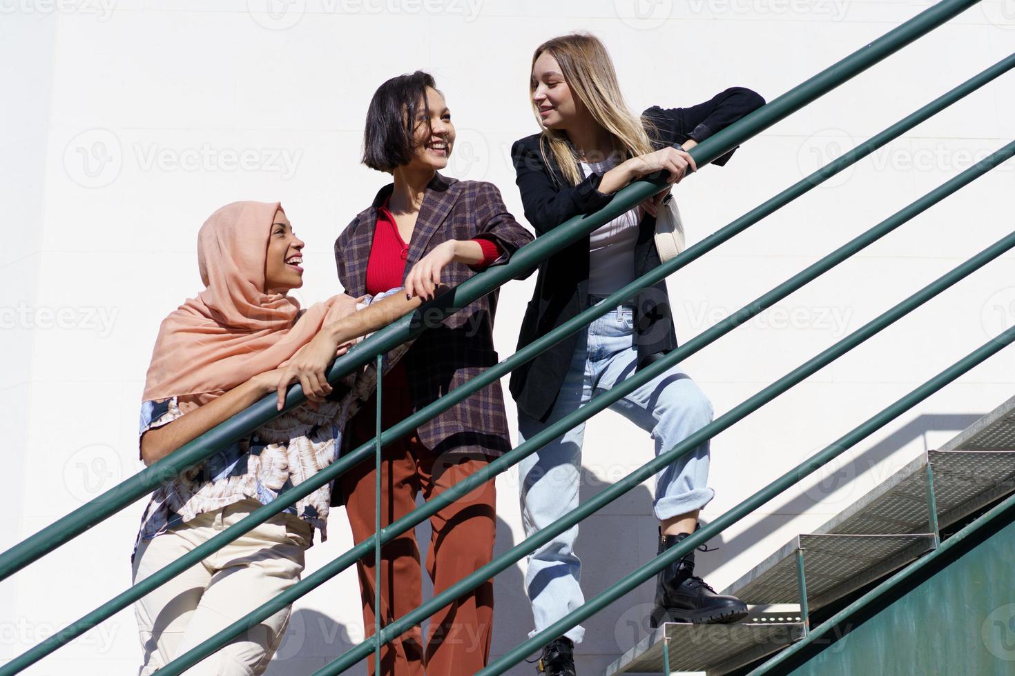 Content young diverse women looking away while standing on stairs in city photo