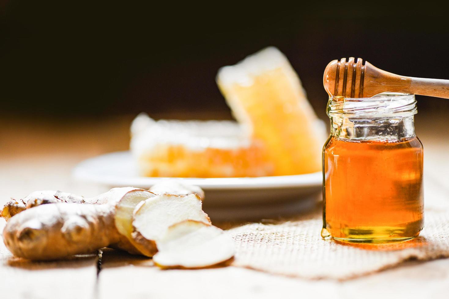 miel en tarro con cucharón de miel, jengibre y sobre madera y panal sobre fondo de placa blanca foto
