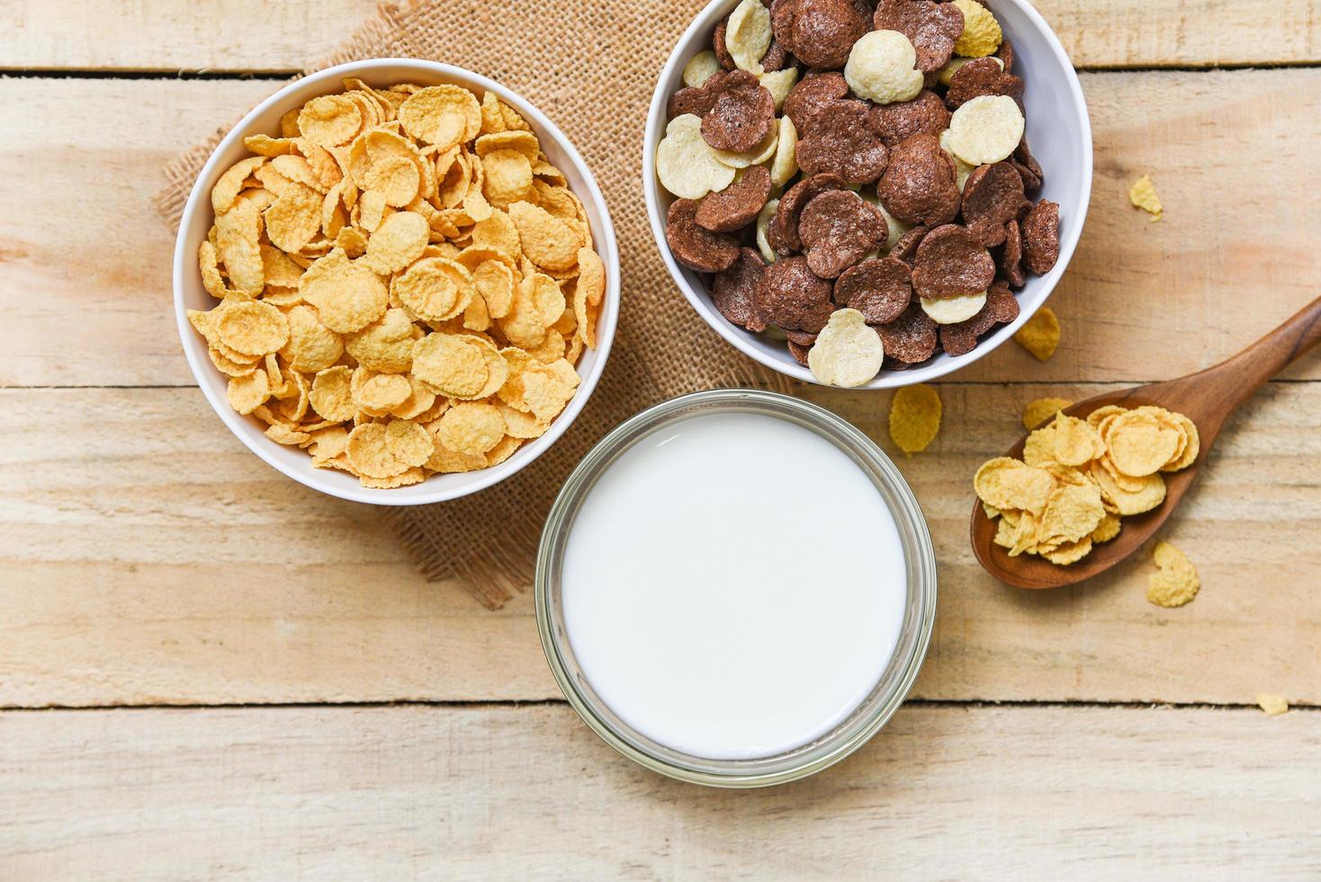 copos de maíz para el desayuno y varios cereales en tazón y taza de leche sobre fondo de madera para alimentos saludables de cereales foto