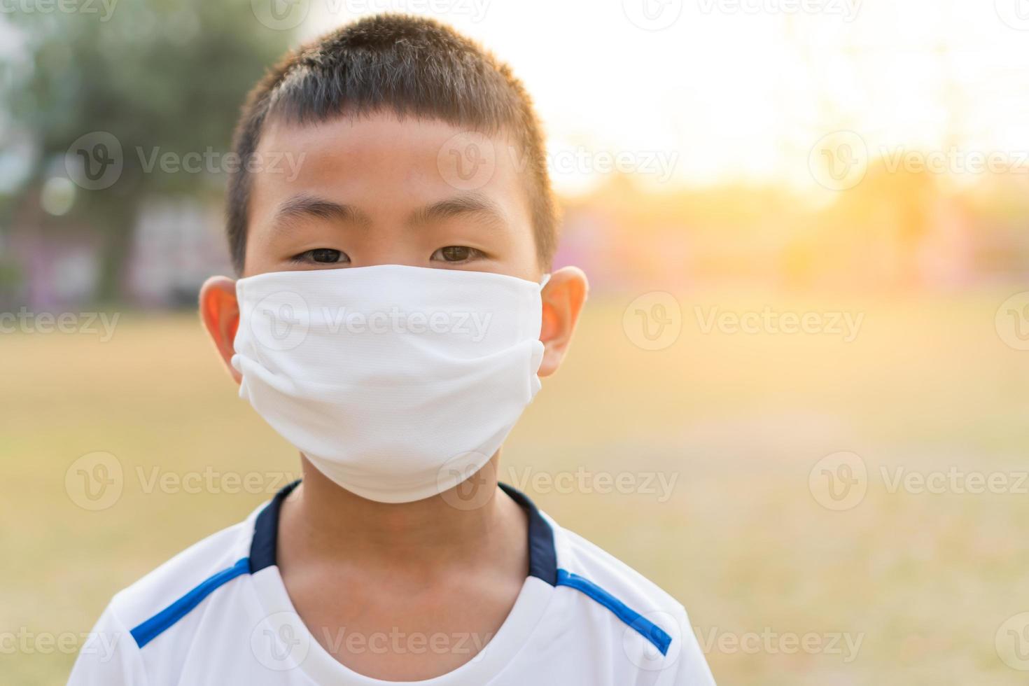 An Asian boy wears a white T-shirt and wearing a white color of face mask in a sunrise natural blurred background. photo