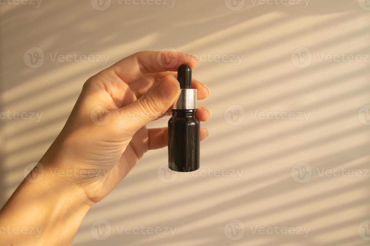 Dropper bottle of cosmetics oil or serum in female hand. Beige monochrome skin care concept photo