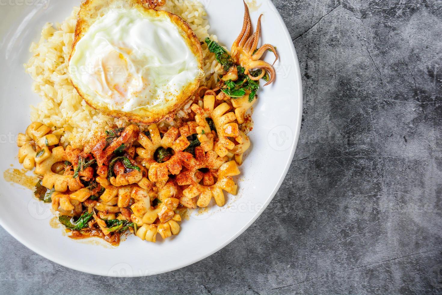 calamares picantes salteados con hojas de albahaca y chile, huevo soleado hacia arriba, servido con arroz integral. plato caliente y picante. foto