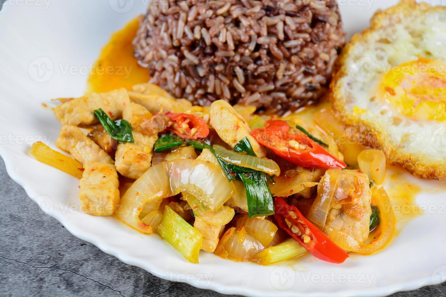 sofría el pollo con cebolla dulce y pimientos, servido con arroz integral y huevo frito en un plato blanco foto