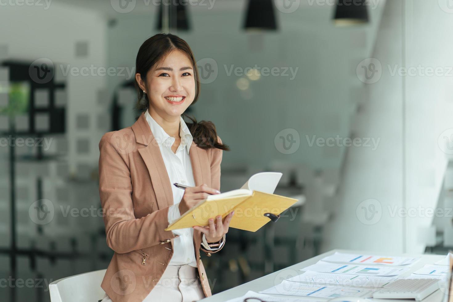 Beautiful smiling Asian woman working at the office, looking at the camera. photo