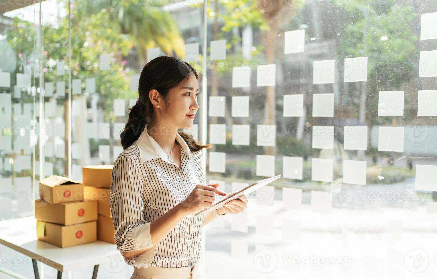 Retrato joven y atractiva propietaria de asia empresa de inicio mira el trabajo de la cámara feliz con la caja en casa prepara la entrega de paquetes en la cadena de suministro de pymes, compras, concepto de comercio omnicanal en línea. foto