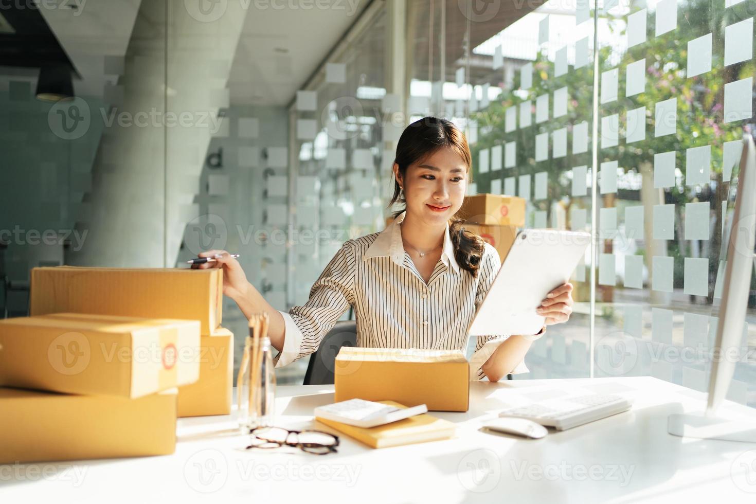 Retrato joven y atractiva propietaria de asia empresa de inicio mira el trabajo de la cámara feliz con la caja en casa prepara la entrega de paquetes en la cadena de suministro de pymes, compras, concepto de comercio omnicanal en línea. foto