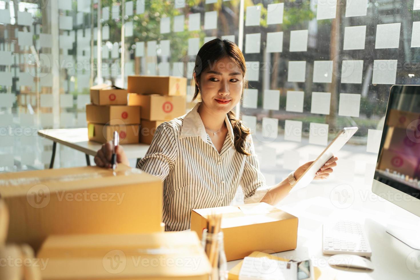 Portrait young attractive asia female owner startup business look at camera work happy with box at home prepare parcel delivery in sme supply chain, procurement, omnichannel commerce online concept. photo