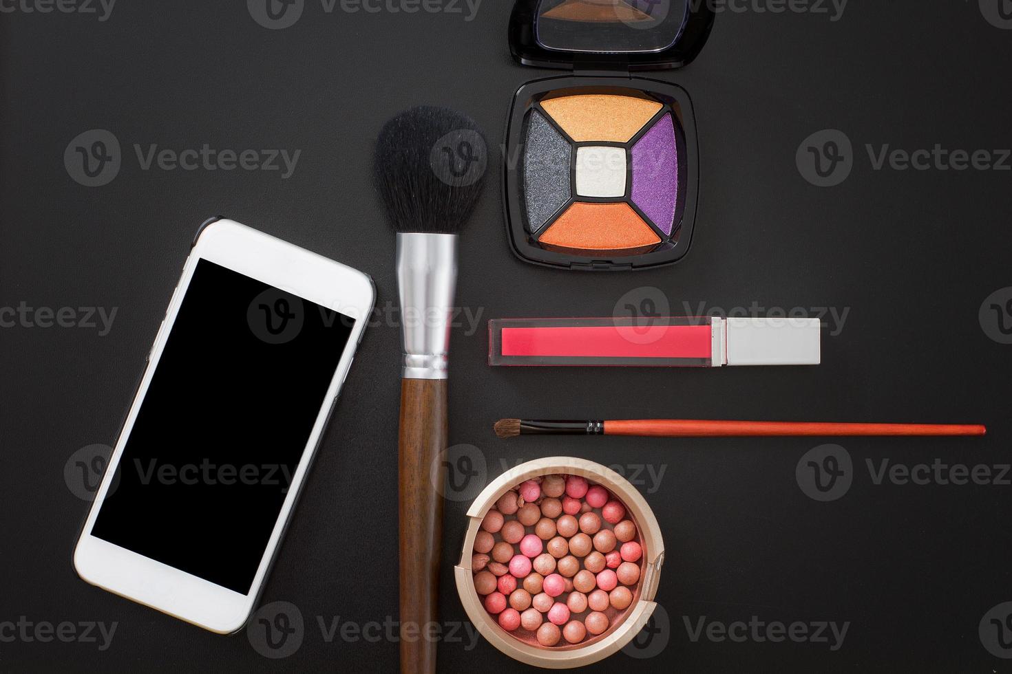 Cosmetic products and accessories on black background. Mobile phone with blank screen. Top view and copy space photo