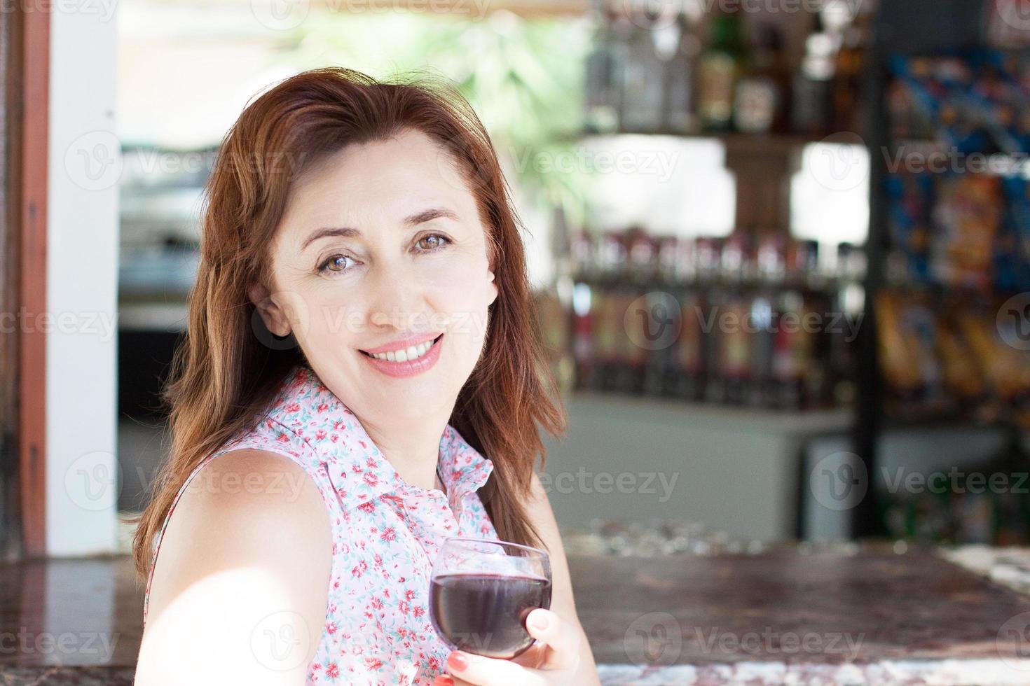 feliz mujer de mediana edad sostenga una copa de vino tinto en el bar del hotel foto