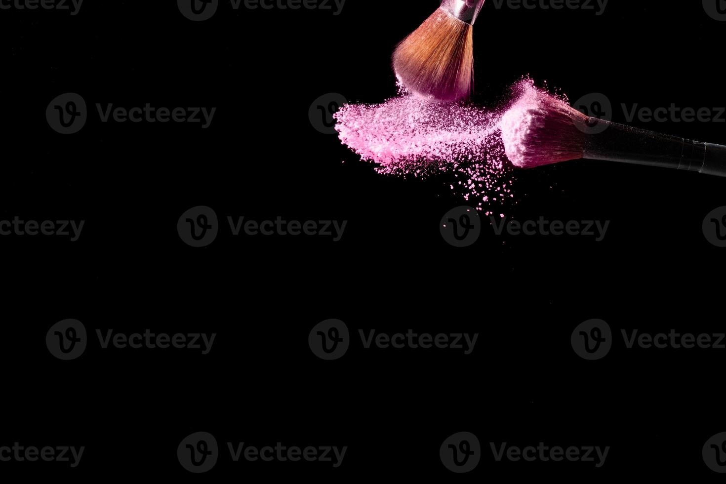 Brushes with pink powder explosion on black background. photo