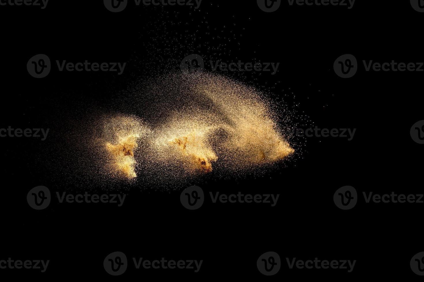 Golden sand explosion isolated on black background. Abstract sand cloud. Golden colored sand splash against dark background. Yellow sand fly wave in the air. photo