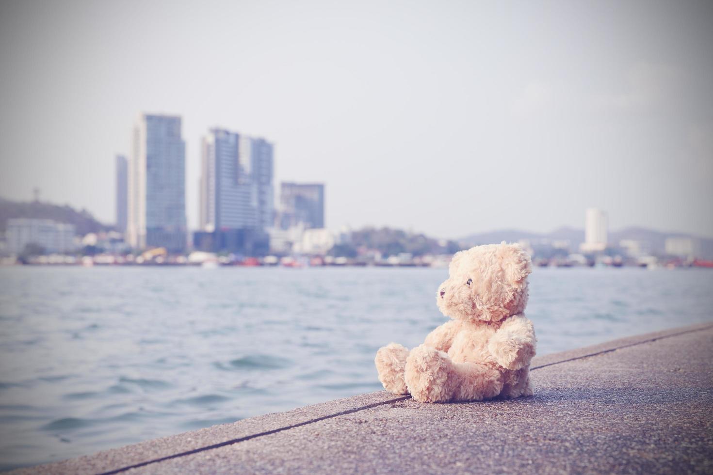 un oso de peluche marrón y esponjoso se sienta en un solo puente mirando al mar con un fondo de espacio de copia. solo, la soledad no tiene sentido. foto