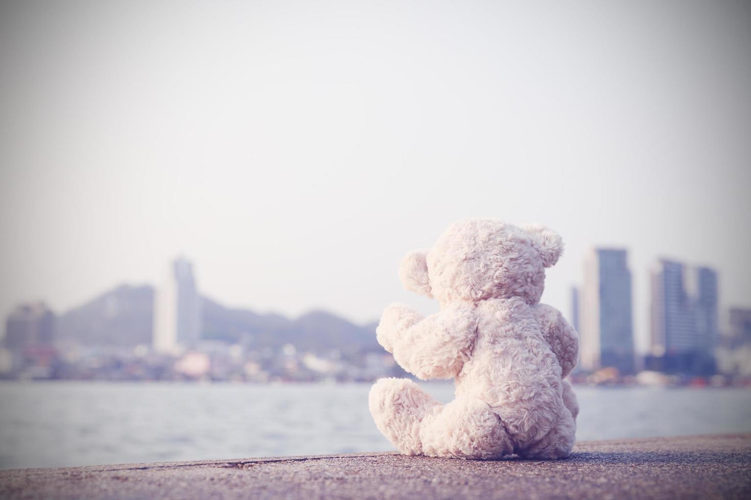 A sad teddy bear sits on a bridge alone looking at the sea in lonely with copy space. Toy, doll, for child. photo