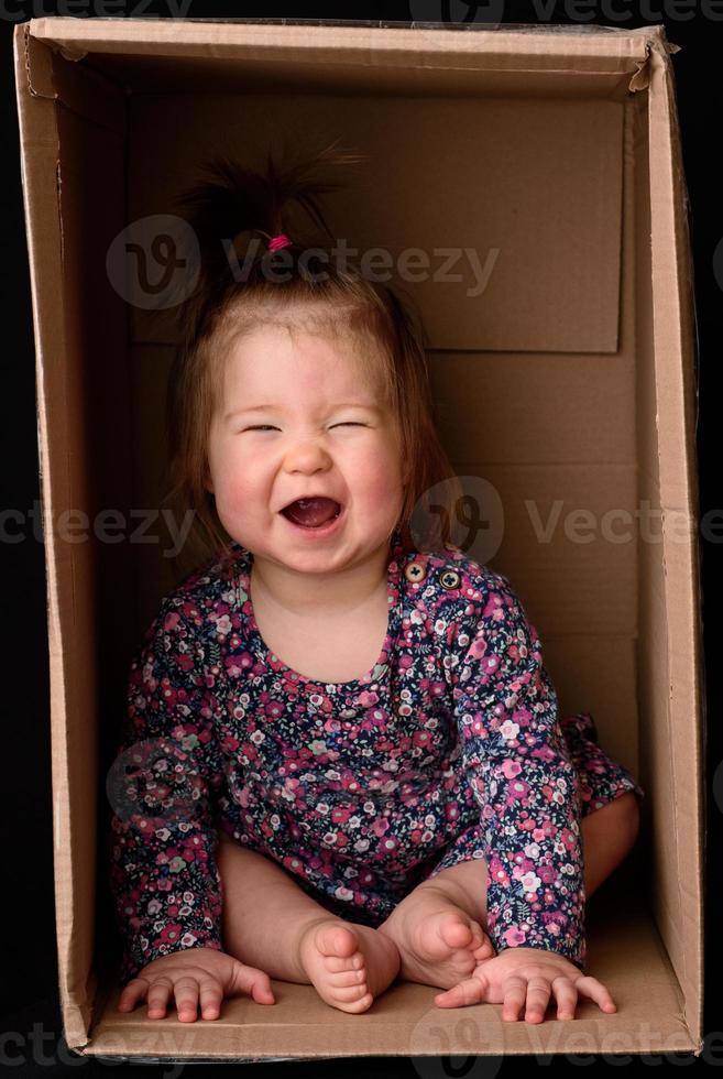 una niña linda y hermosa se sienta en una caja. foto