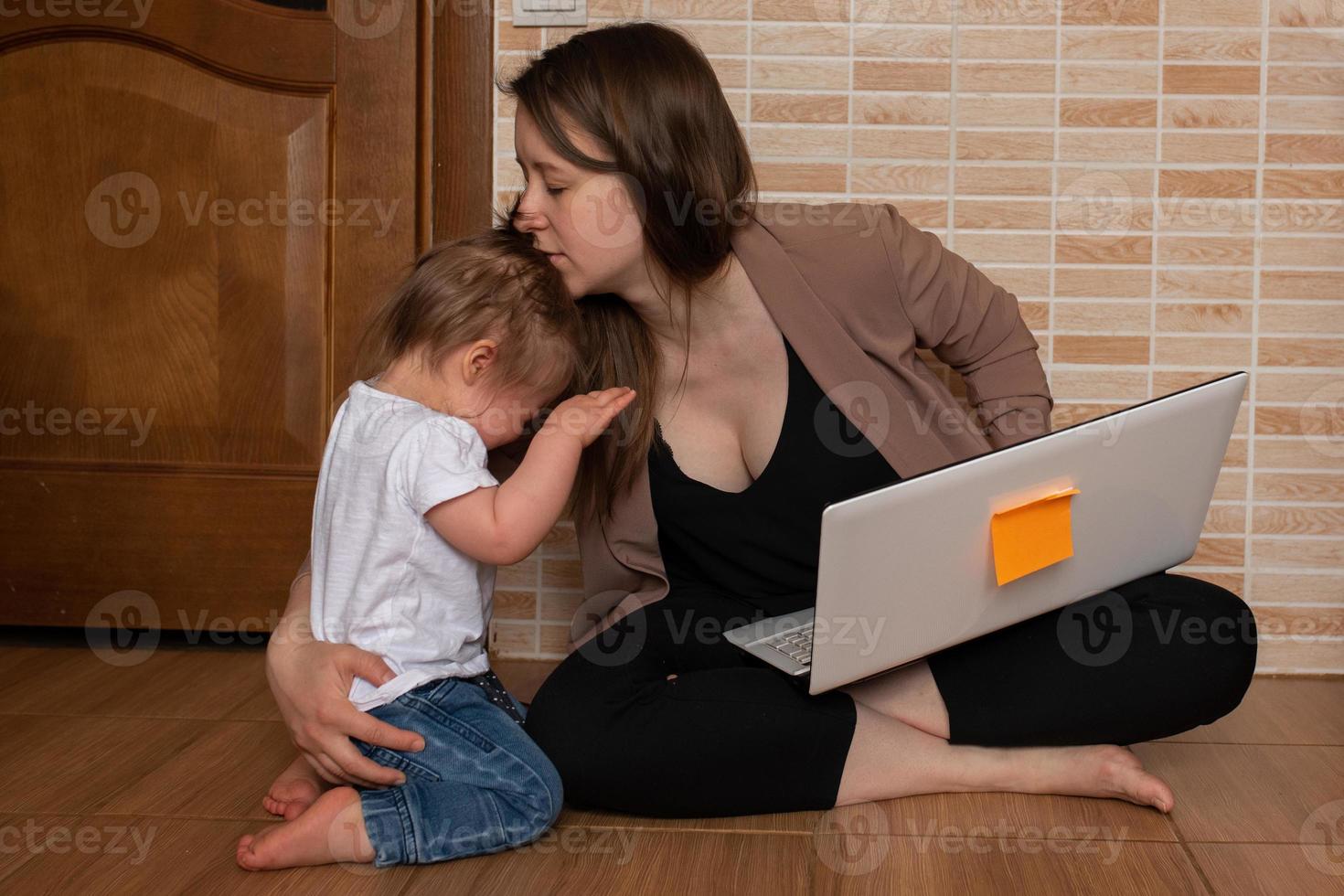 Young beautiful mother is trying to work remotely. Her little daughter is bothering her. photo