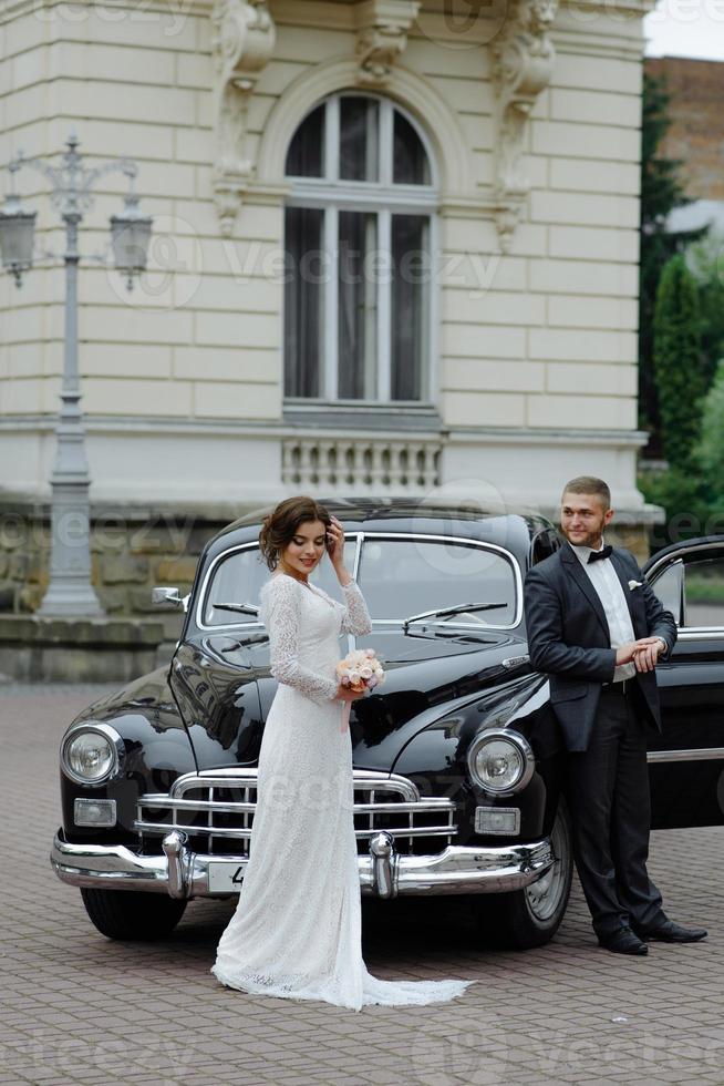 elegant gorgeous bride and handsome groom embracing in stylish black car in light. unusual view from back. luxury wedding couple in retro style. photo
