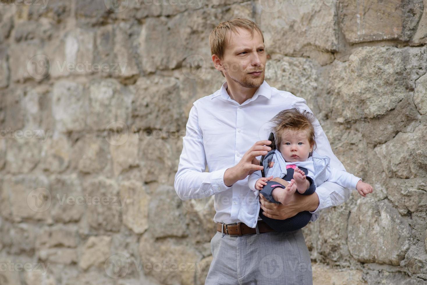 A young father is talking on a cell phone and holds his little daughter in his arms. copy space photo