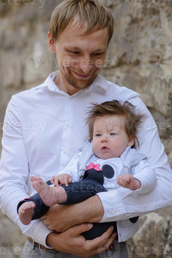 portrait of young father holding crying baby girl over white brick wall photo