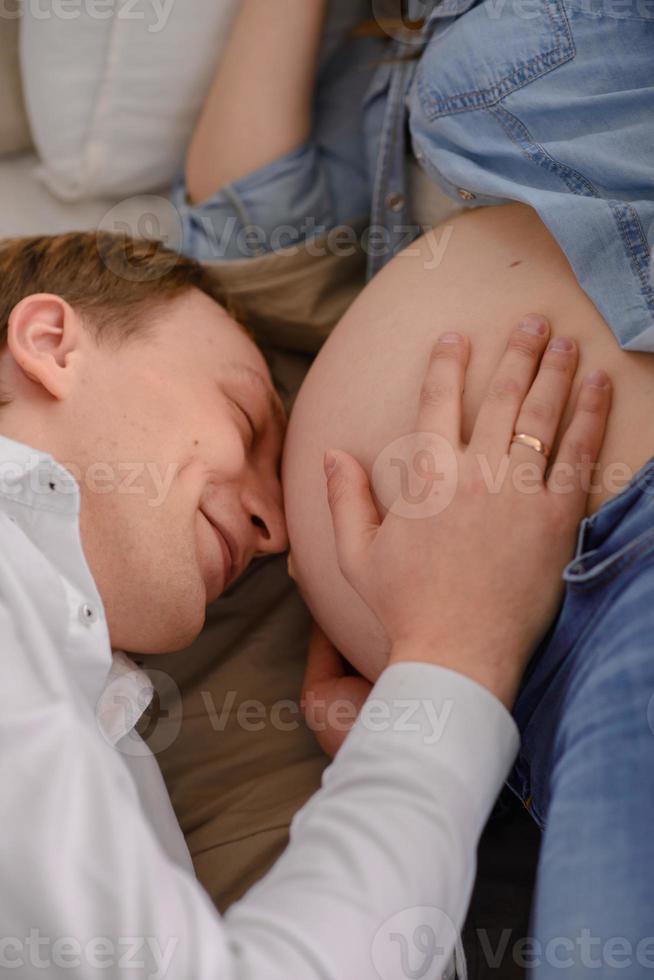 el futuro padre escucha como su hijo golpea en el vientre de su esposa embarazada. foto